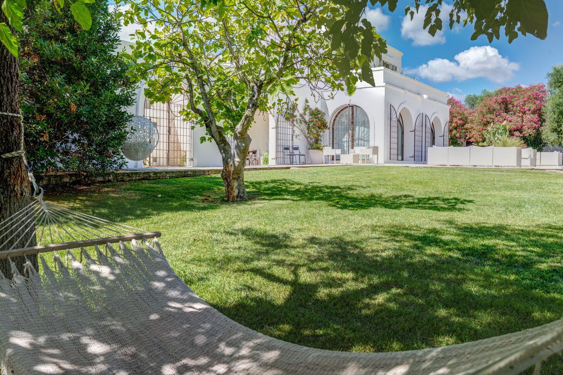 A grassy courtyard with a hammock, a tree, and a building with arched windows and a white facade.