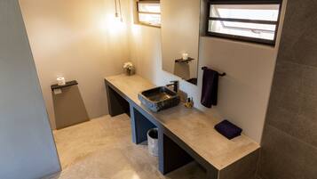 A modern bathroom with a stone sink, a mirror, a towel rack, and a small window.