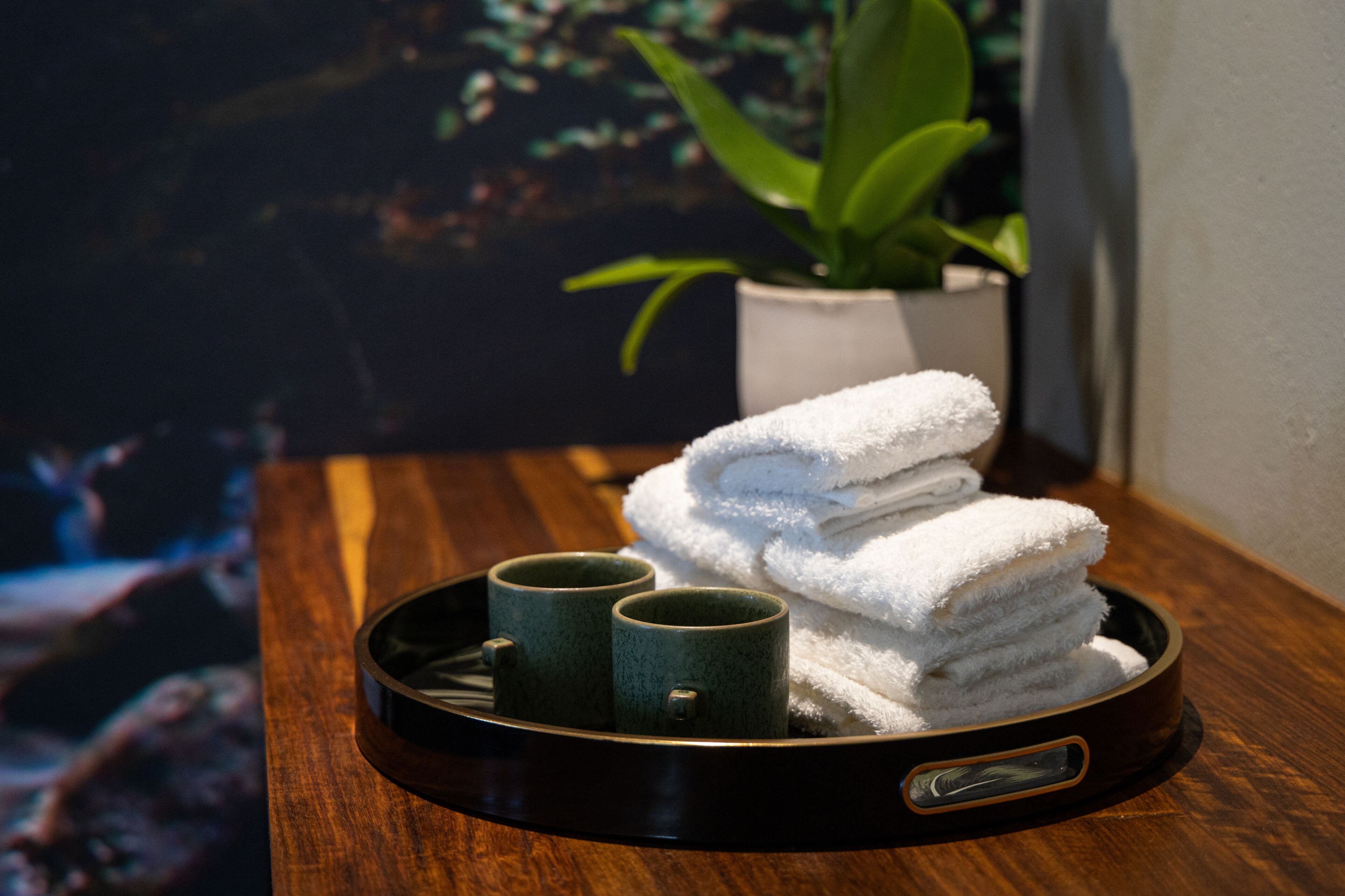 A tray with folded towels and two green mugs on a wooden surface.