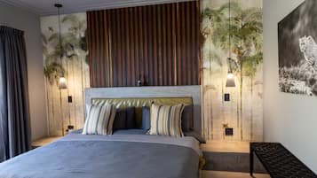 Un dormitorio moderno con una cama grande, almohadas a rayas, un cabecero de madera y luces fijadas a la pared.