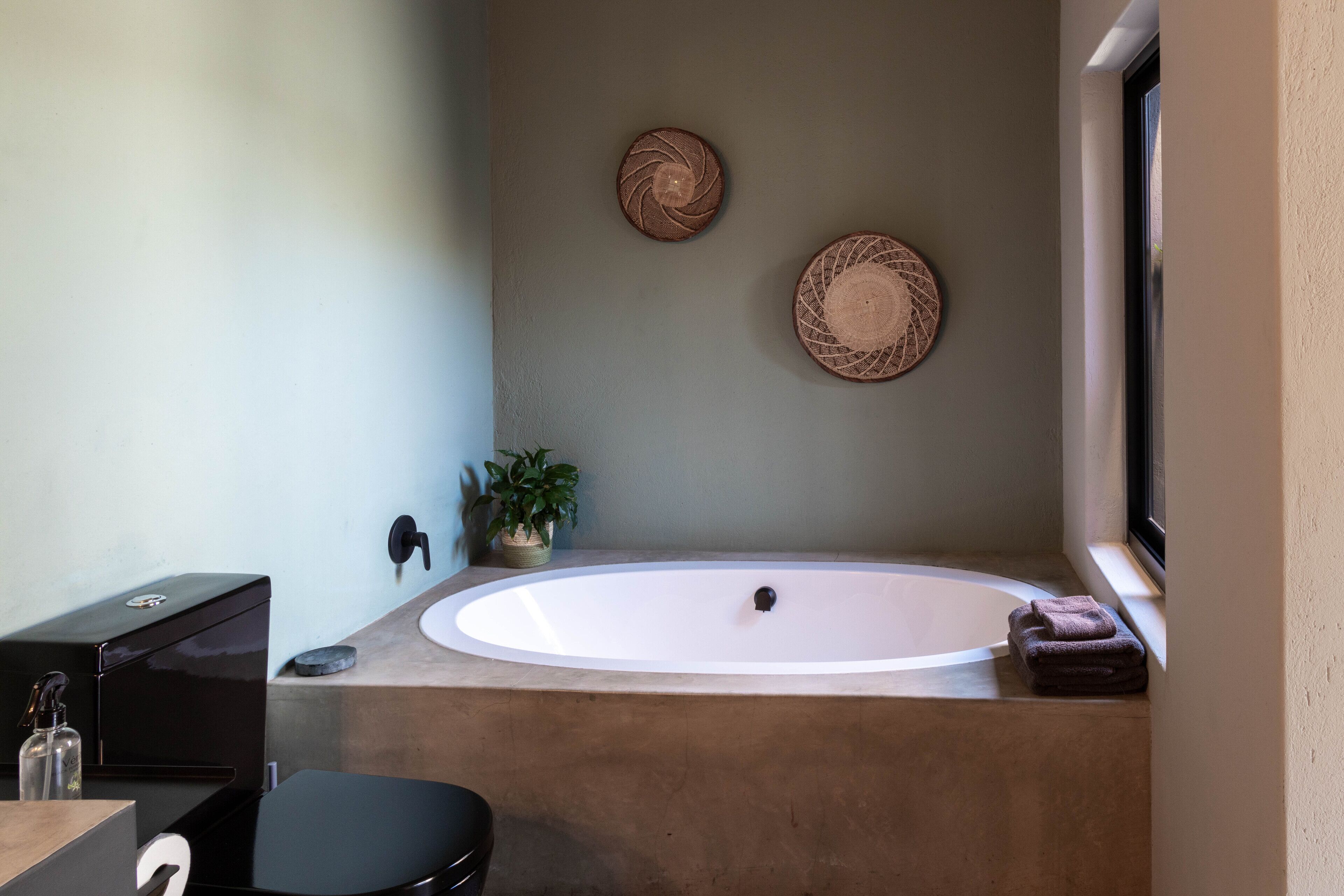 Une salle de bain avec une baignoire, un lavabo et des toilettes. On y trouve deux éléments de décoration murale en fibres tressées et une plante en pot.