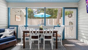 Une terrasse couverte avec une table et des chaises, un parasol bleu et un canapé en osier agrémenté d’un coussin en forme d’étoile de mer.