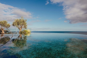 An infinity pool with clear blue water, surrounded by trees and a view of the ocean. - The Reserve - The Leading Hotels of the World - Savoy Signature (Funchal)