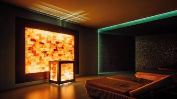 A modern spa room with a heated stone wall, a massage table, and a small seating area.