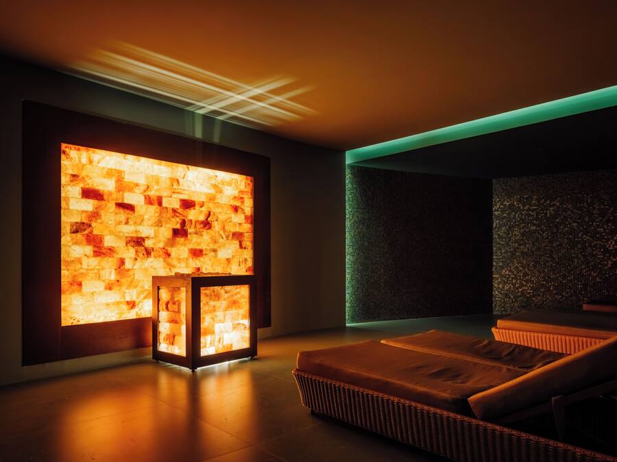 A modern spa room with a heated stone wall, a massage table, and a small seating area.