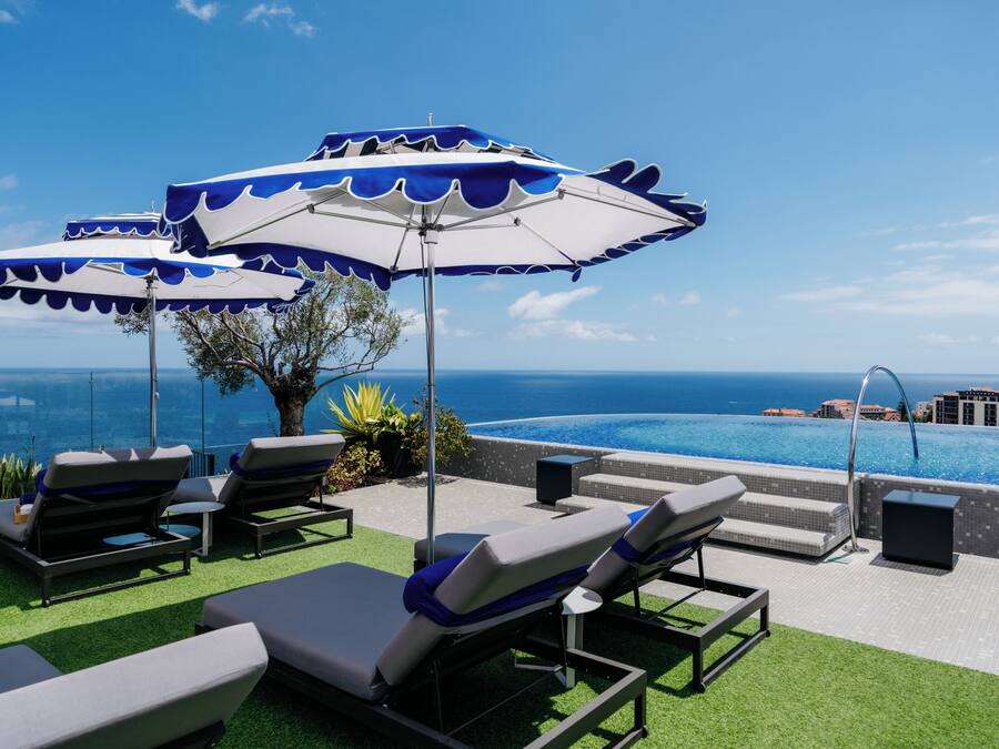 Zona de piscina en la azotea con sillones y sombrillas, con vista a un océano azul y despejado.