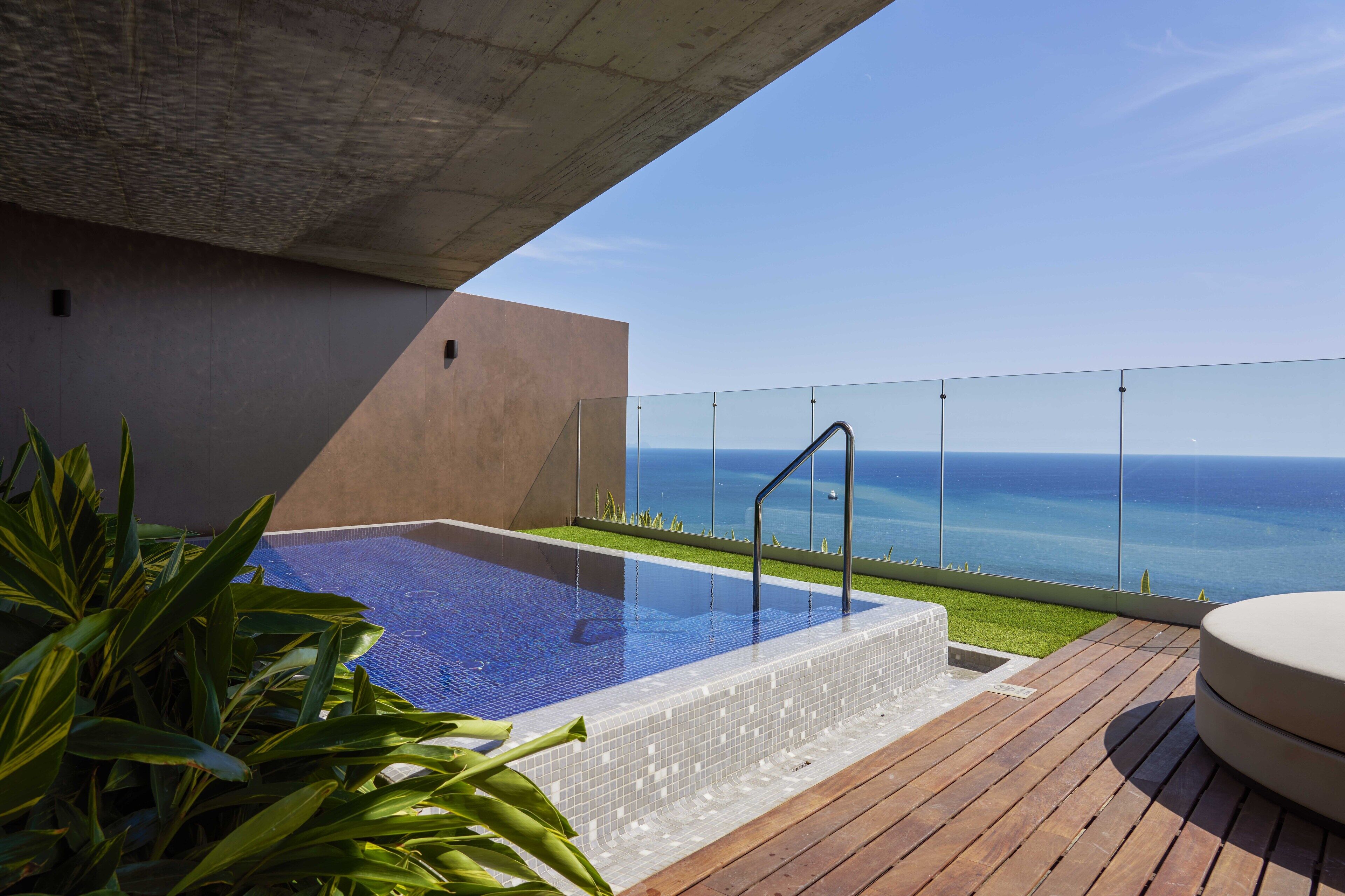 Ein Pool auf dem Dach mit freiem Blick auf den Ozean, umgeben von Holzterrassen und Blumentöpfen.