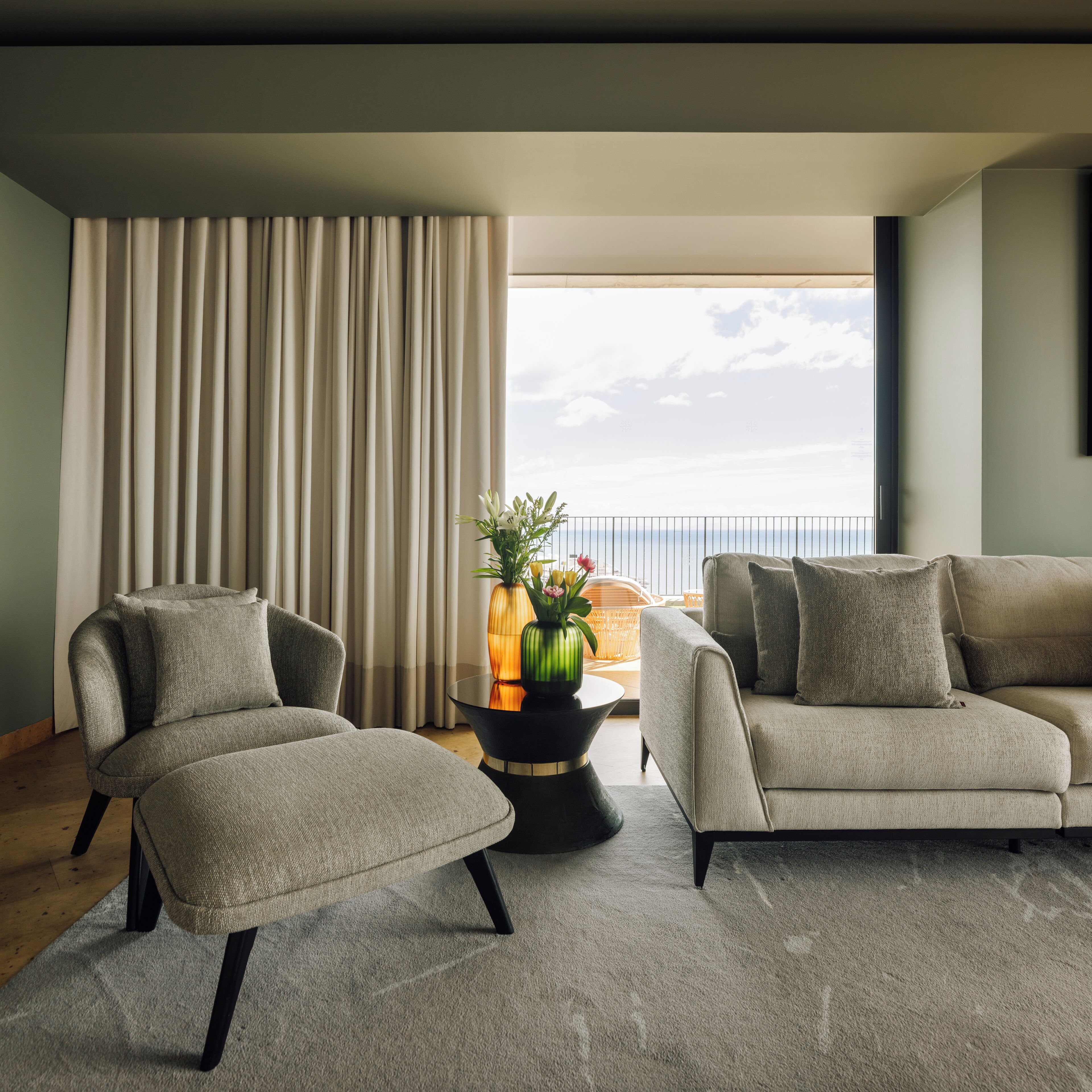 A modern living room with two grey sofas, a black coffee table, and a large window with curtains.