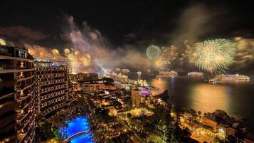 Un hotel con varios pisos, piscina y vistas a fuegos artificiales sobre el agua.