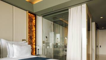A modern hotel room with a large bed, a glass shower enclosure, and a view of the city.