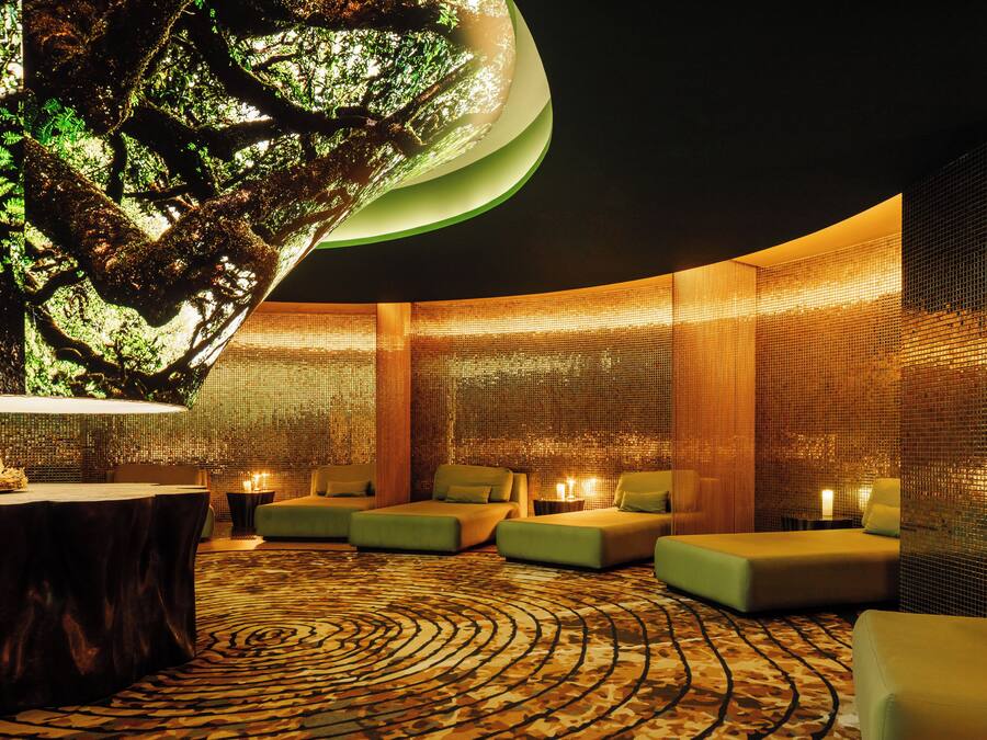 A modern spa room with a circular seating area, a large tree sculpture, and a patterned carpet.