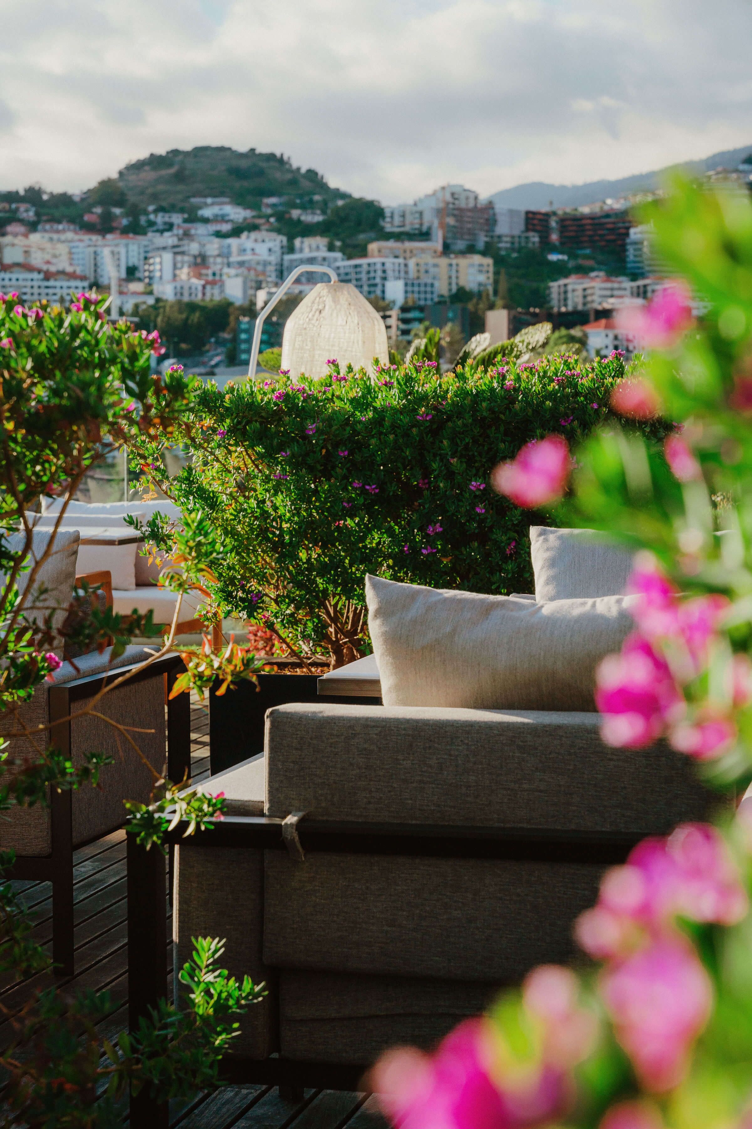 A rooftop terrace with outdoor furniture, a view of a cityscape, and a hill in the background.