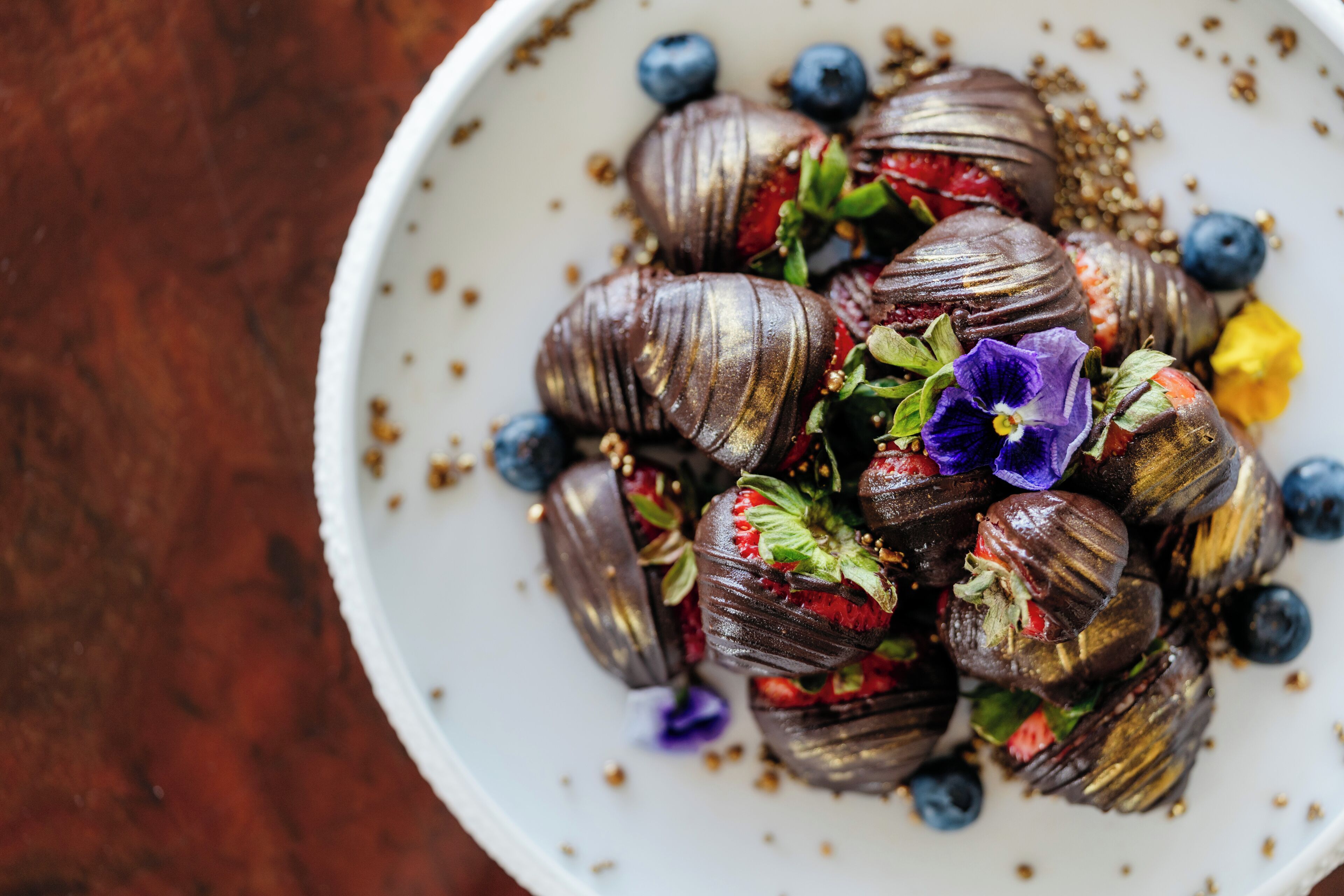 Een schaal met chocoladebedekte aardbeien, bosbessen en bloemen.