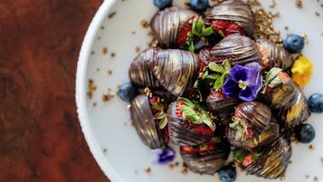 Een schaal met chocoladebedekte aardbeien, bosbessen en bloemen.