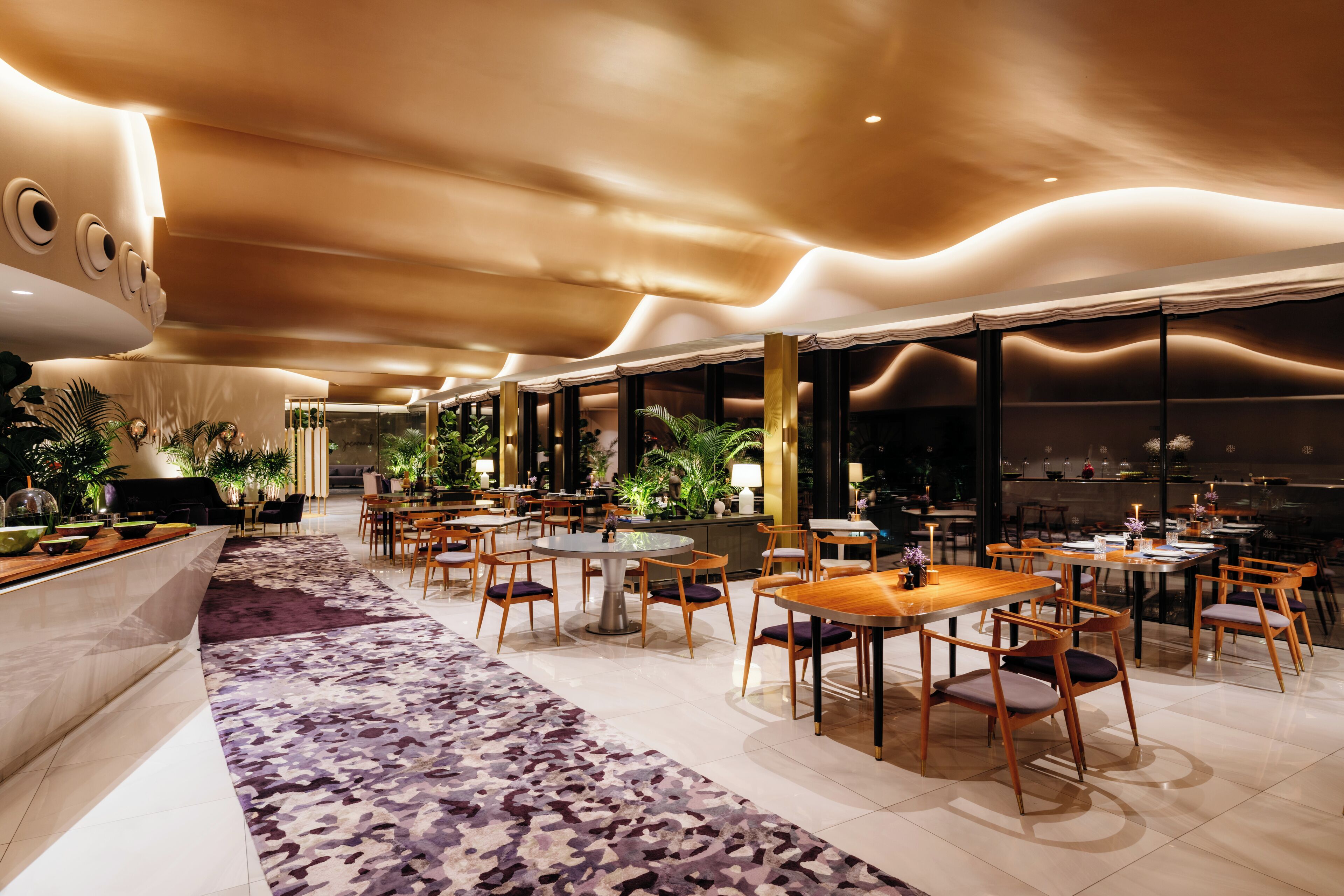 Un hall d’hôtel moderne avec un espace salon central, un comptoir d’accueil et une moquette à motifs.