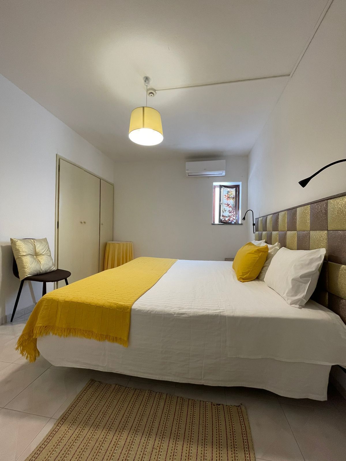 Ein Schlafzimmer mit Bett, Sessel, Fenster und Klimaanlage.