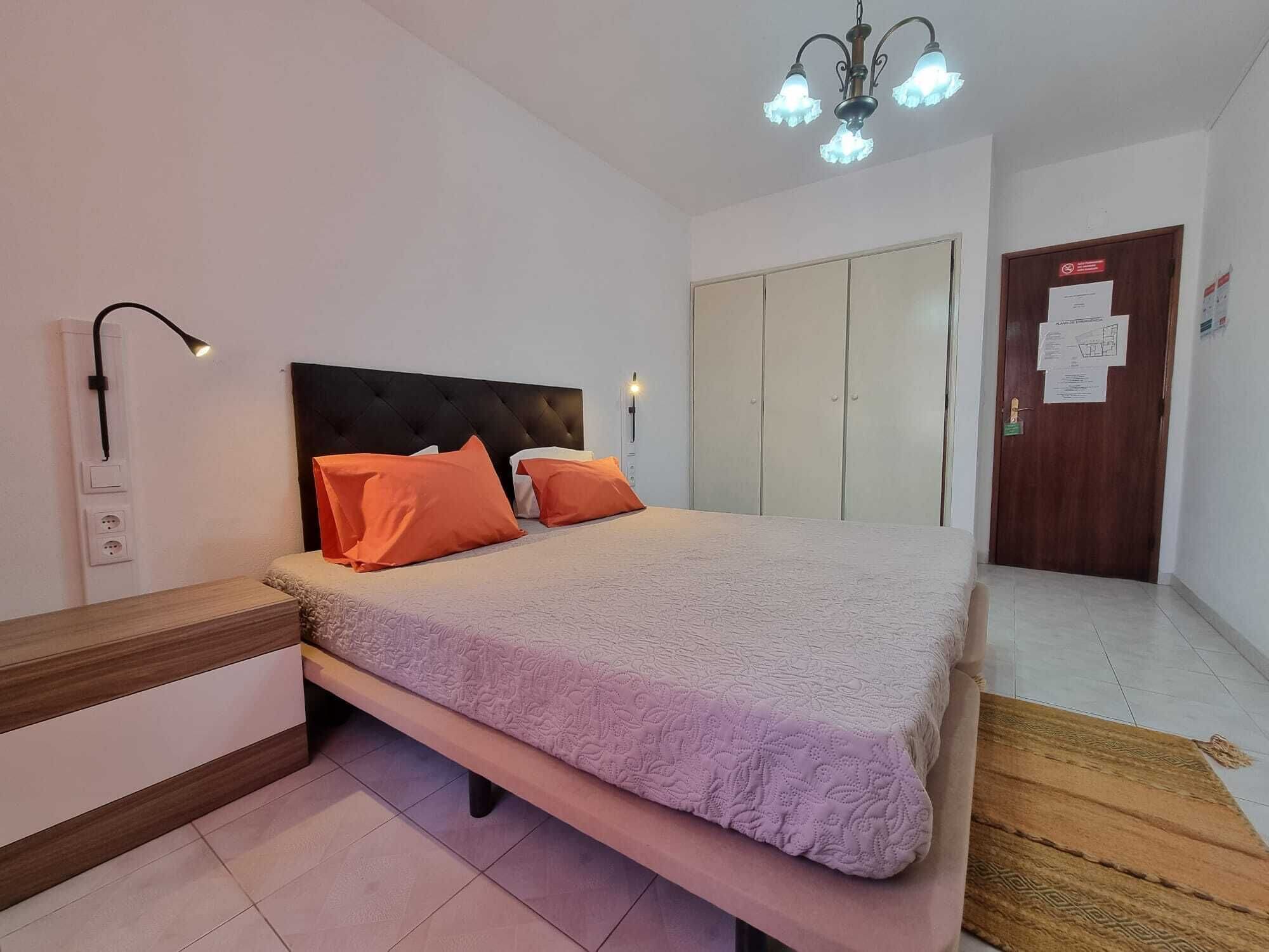 Un dormitorio con cama, mesita de noche, lámpara, armario y una puerta con un aviso.