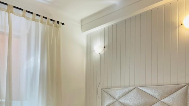 A neatly made bed with a patterned bedspread, a headboard with a diamond pattern, and a bedside table with a lamp.