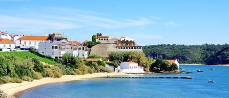 A coastal town with white buildings, a prominent fort, and a beach.