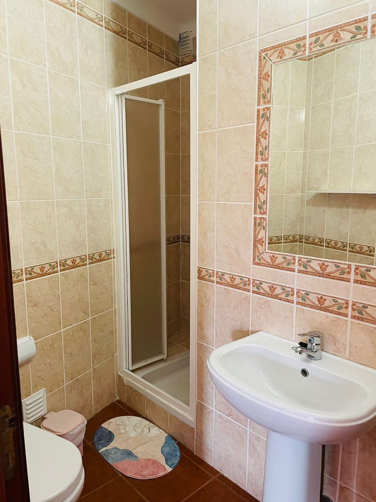Une salle de bain équipée d’une douche, de toilettes, d’un lavabo et d’un miroir agrémenté de carreaux décoratifs.
