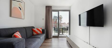 A modern living room with a grey sofa, a flat-screen TV mounted on the wall, and a sliding glass door leading to an outdoor area.