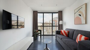 Un salon moderne avec un canapé gris, une table basse ronde et un téléviseur à écran plat fixé au mur.