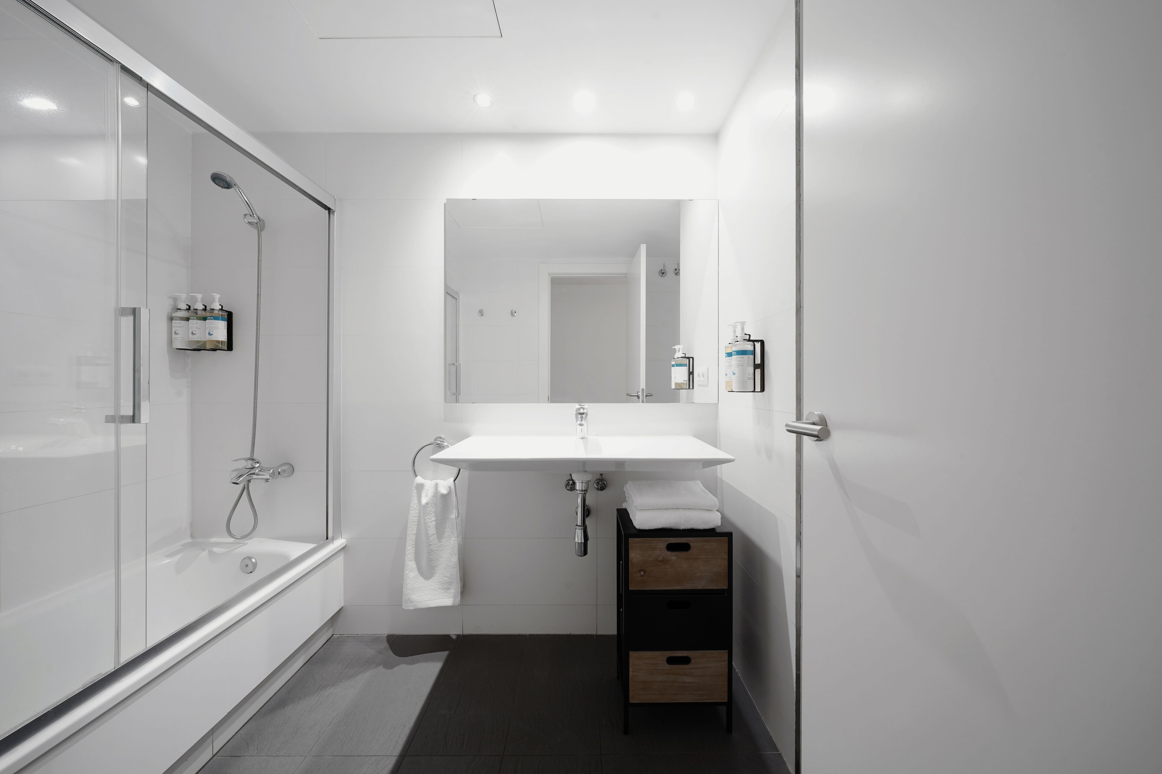 Un baño moderno con ducha envuelta en vidrio, un lavamanos blanco y un mueble de madera.