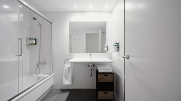 Un baño moderno con ducha envuelta en vidrio, un lavamanos blanco y un mueble de madera.