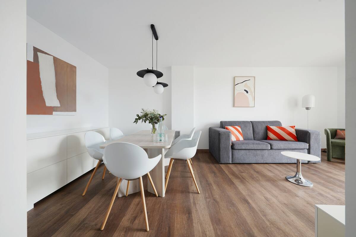 Uma sala de estar moderna com um sofá cinzento, cadeiras brancas, uma mesa de jantar e um lustre.