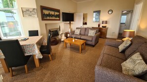 Een woonkamer met een bank, salontafel en stoelen, een open haard, een televisie en kunstwerken aan de muren.