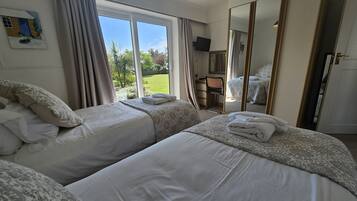 Ein Hotelzimmer mit zwei Betten, einem großen Fenster, einem Spiegel und einem Fernseher.