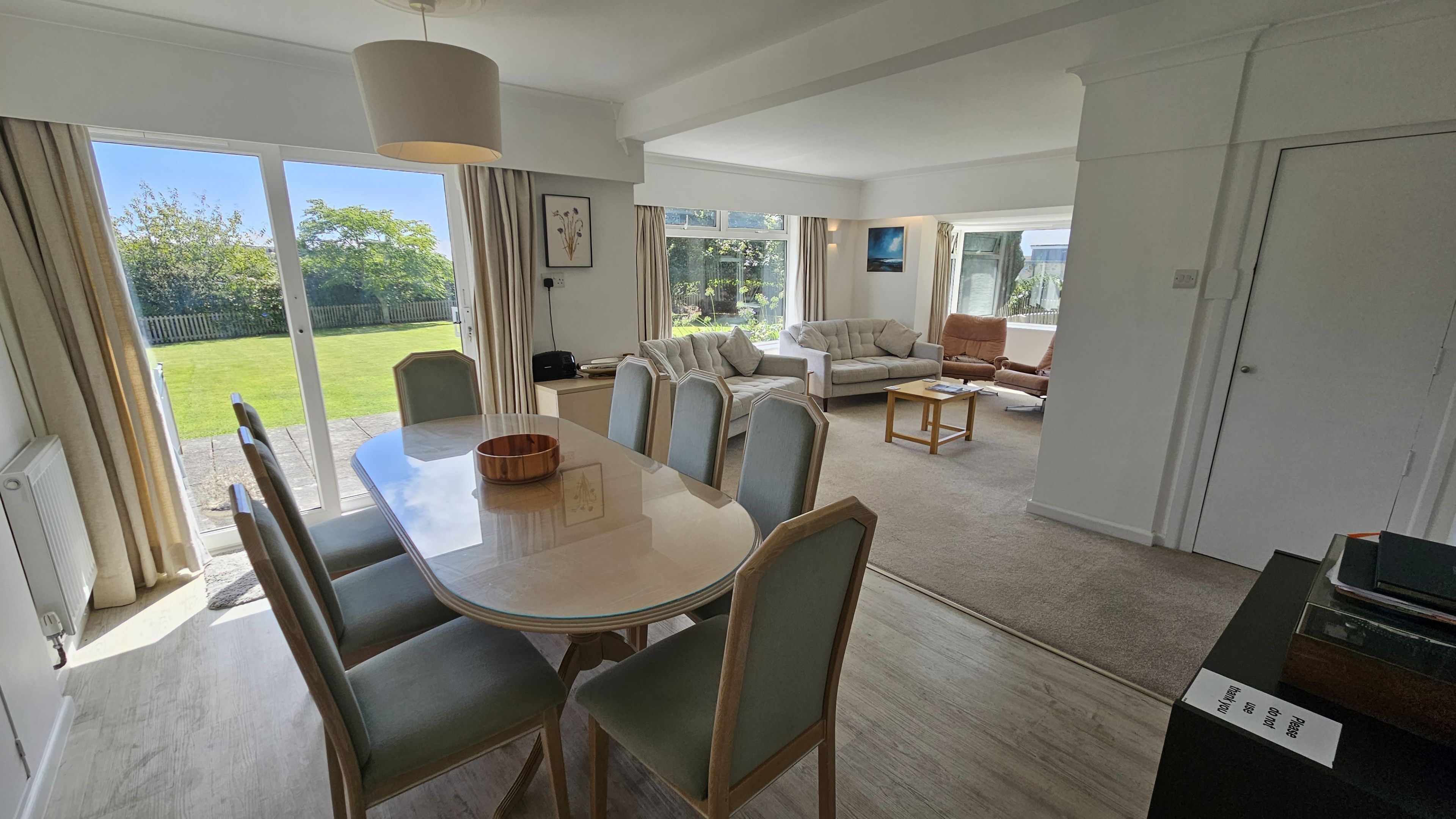 Un vaste espace de vie comprenant un coin repas avec une table, des chaises et un canapé. De grandes fenêtres offrent une vue sur un jardin.