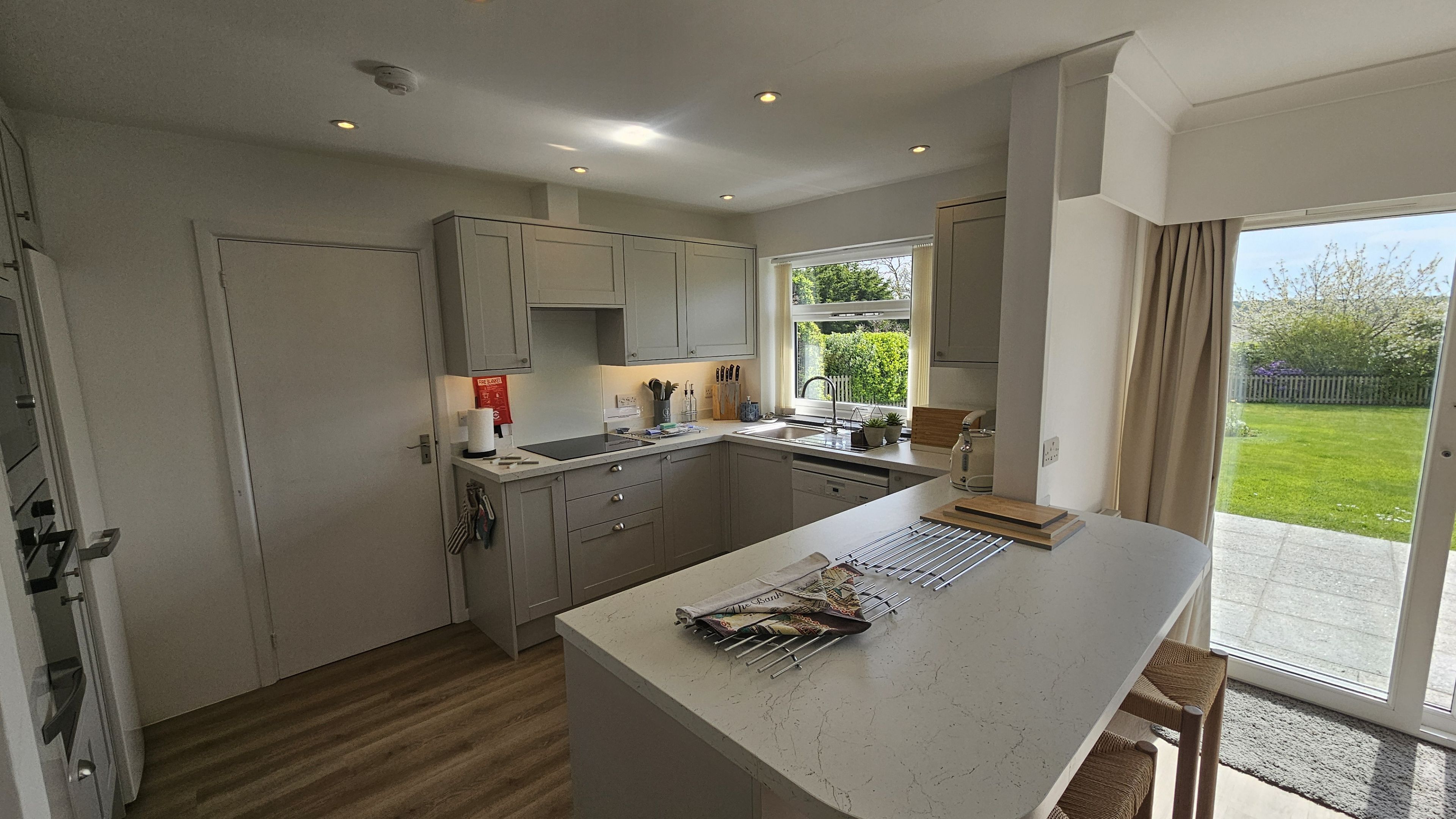 A modern kitchen with grey cabinets, a central island, and a view of a garden through a sliding glass door.