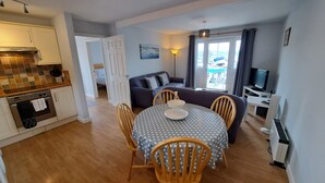 Een knus woongedeelte met een kitchenette, een eethoek met tafel en stoelen, een bank, een televisie en uitzicht door een raam.