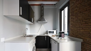 A compact kitchen with a washing machine, a microwave, and a coffee maker. - Numa | Lustre Apartments (Barcelona)