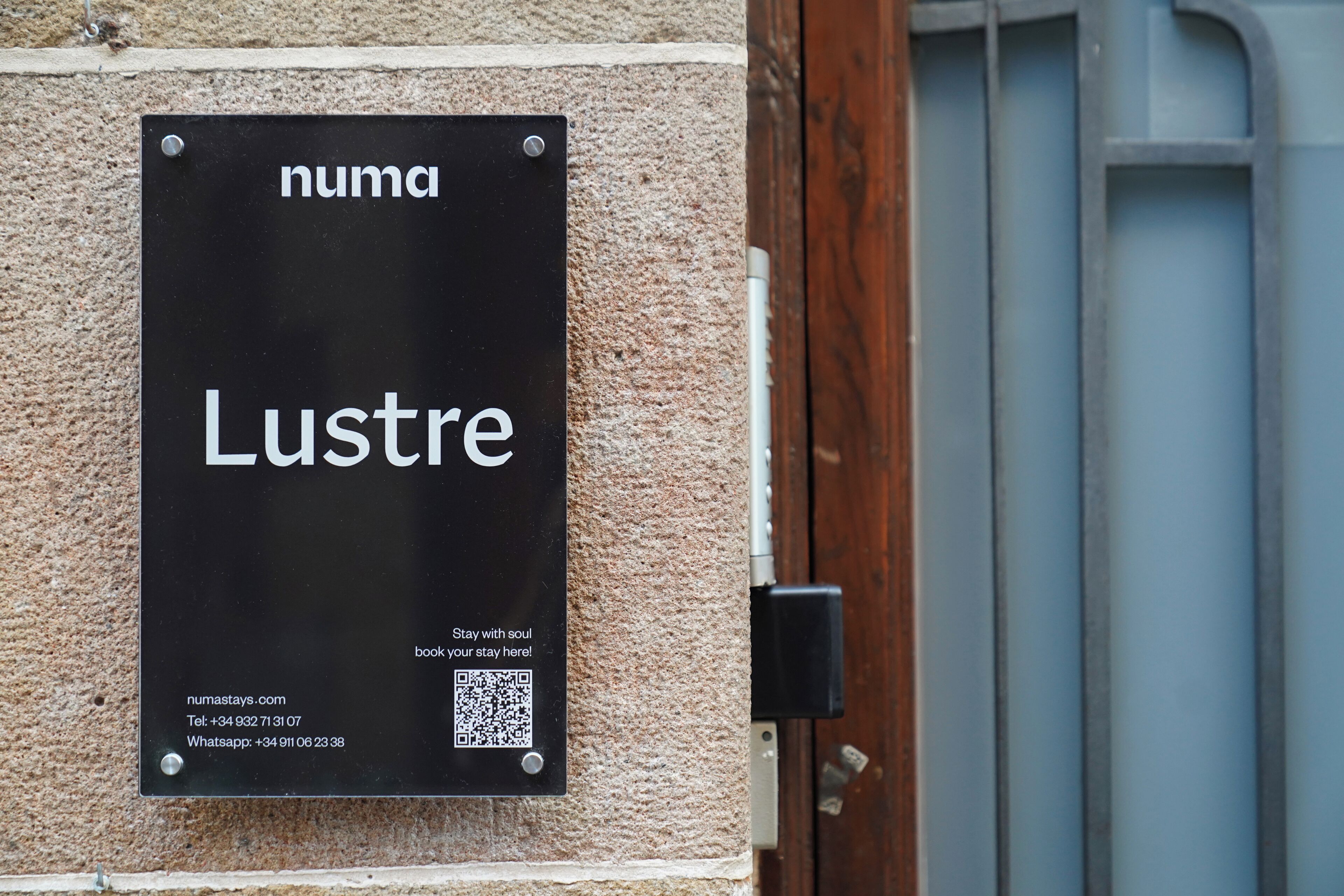 A black sign with white text on a textured wall, including contact information and a QR code.
