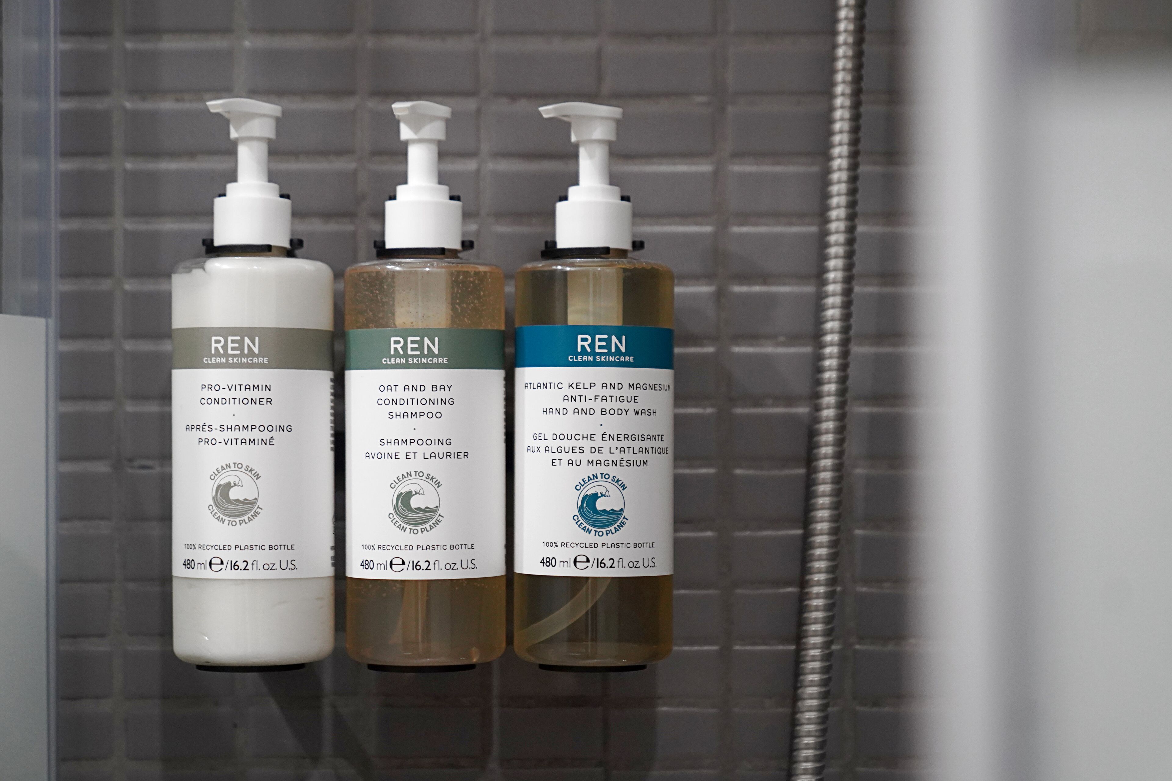 Three bottles of REN skincare products on a tiled wall.