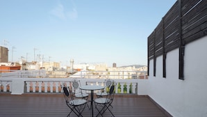 A rooftop terrace with a table and chairs, a white railing, and a view of the cityscape. - Numa | Lustre Apartments (Barcelona)