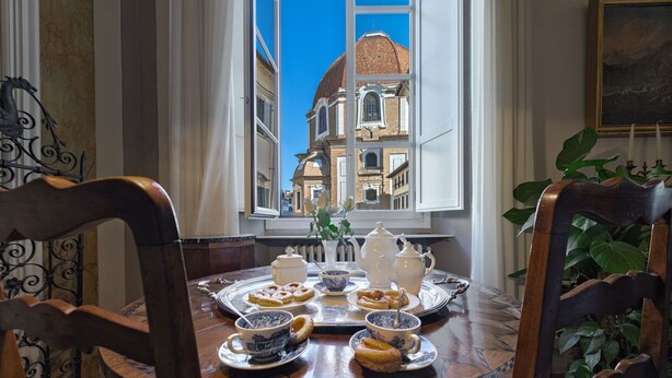A dining table with pastries and tea set, a window with a view of historic buildings, and ornate chairs. - Apartment in Florence with 3 bedrooms sleeps 5 (Florence)