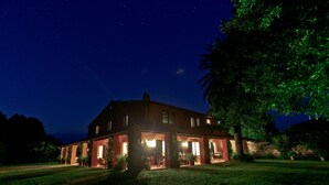 A large, two-story house with a well-lit front porch and a lawn in the foreground.