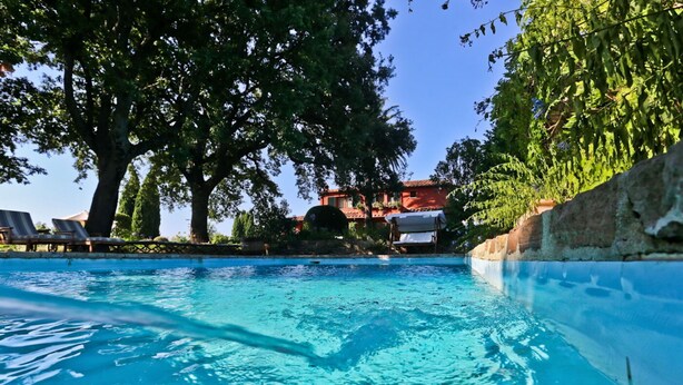 A swimming pool with lounge chairs and a red building in the background.