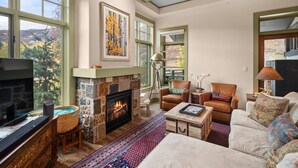 A spacious living room with a fireplace, comfortable seating, and large windows offering a view of the outdoors.