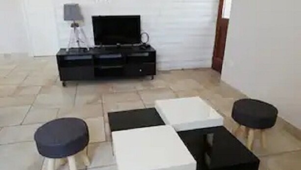 Un salon comprenant un meuble de rangement noir pour appareils électroniques, un téléviseur à écran plat et une table basse au motif noir et blanc. On y trouve également deux tabourets avec des assises noires.