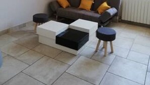 Un salon avec un canapé gris, deux poufs noirs et une table basse blanche.