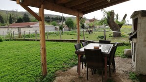 Un espace extérieur abrité, avec une table et des chaises, un chemin de terre et un champ clôturé où se trouvent des chevaux.