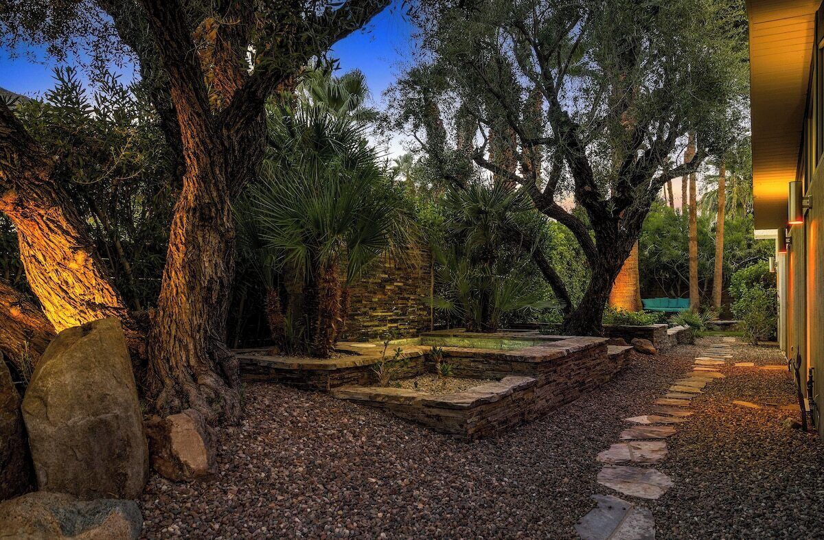 A garden pathway with stone steps, surrounded by large trees and a building with warm lighting.