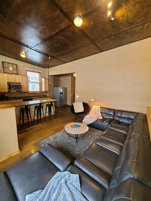 A modern living room with a black leather sofa, a round coffee table, and a kitchen area with wooden cabinets and a refrigerator. - Cozy and Charming Vacation Rental Near Downtown Fargo (Fargo)