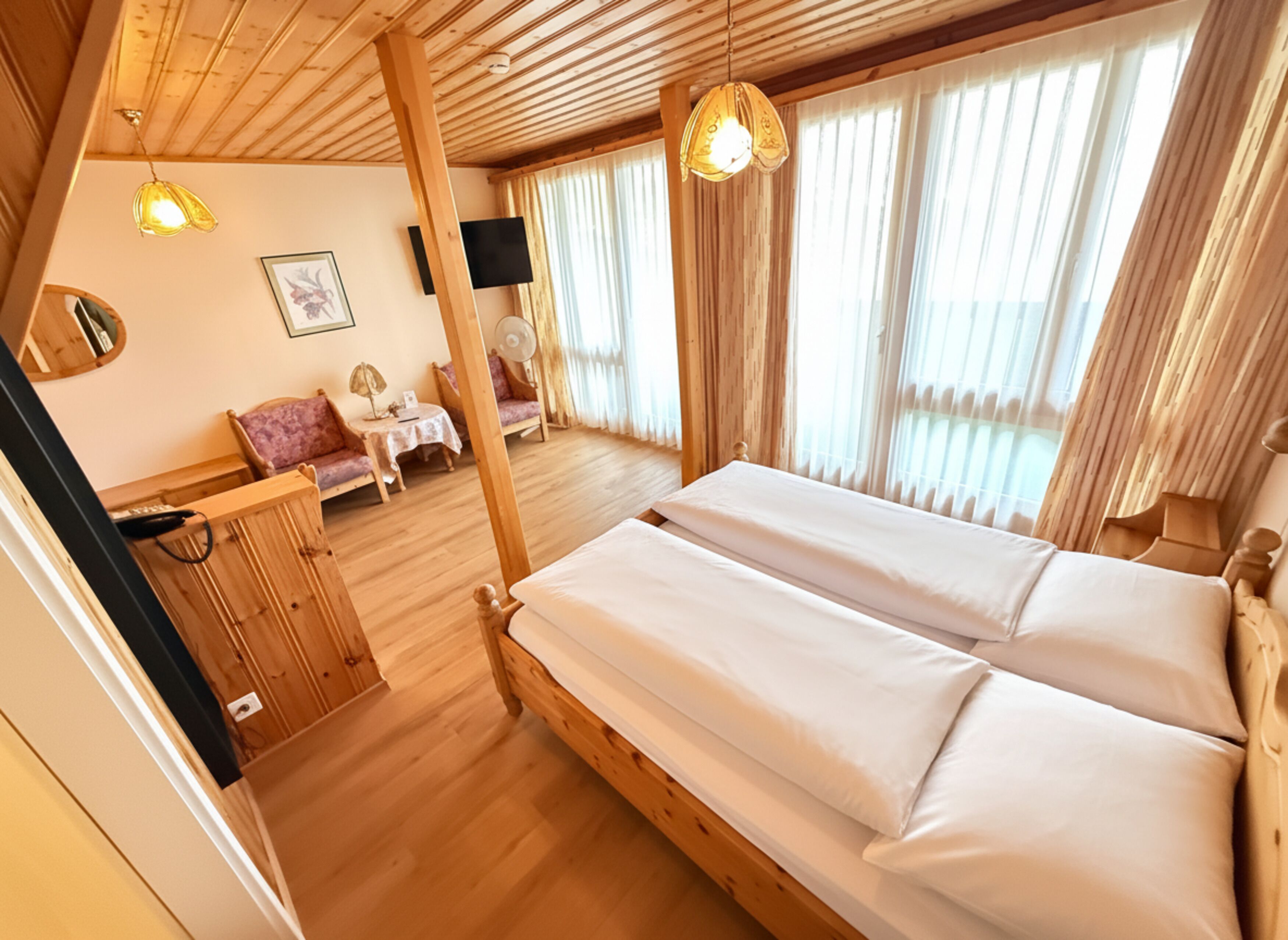 A wooden room with a bed, a small table, and a chair.