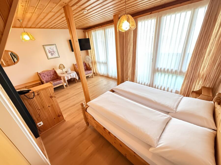A wooden room with a bed, a small table, and a chair.