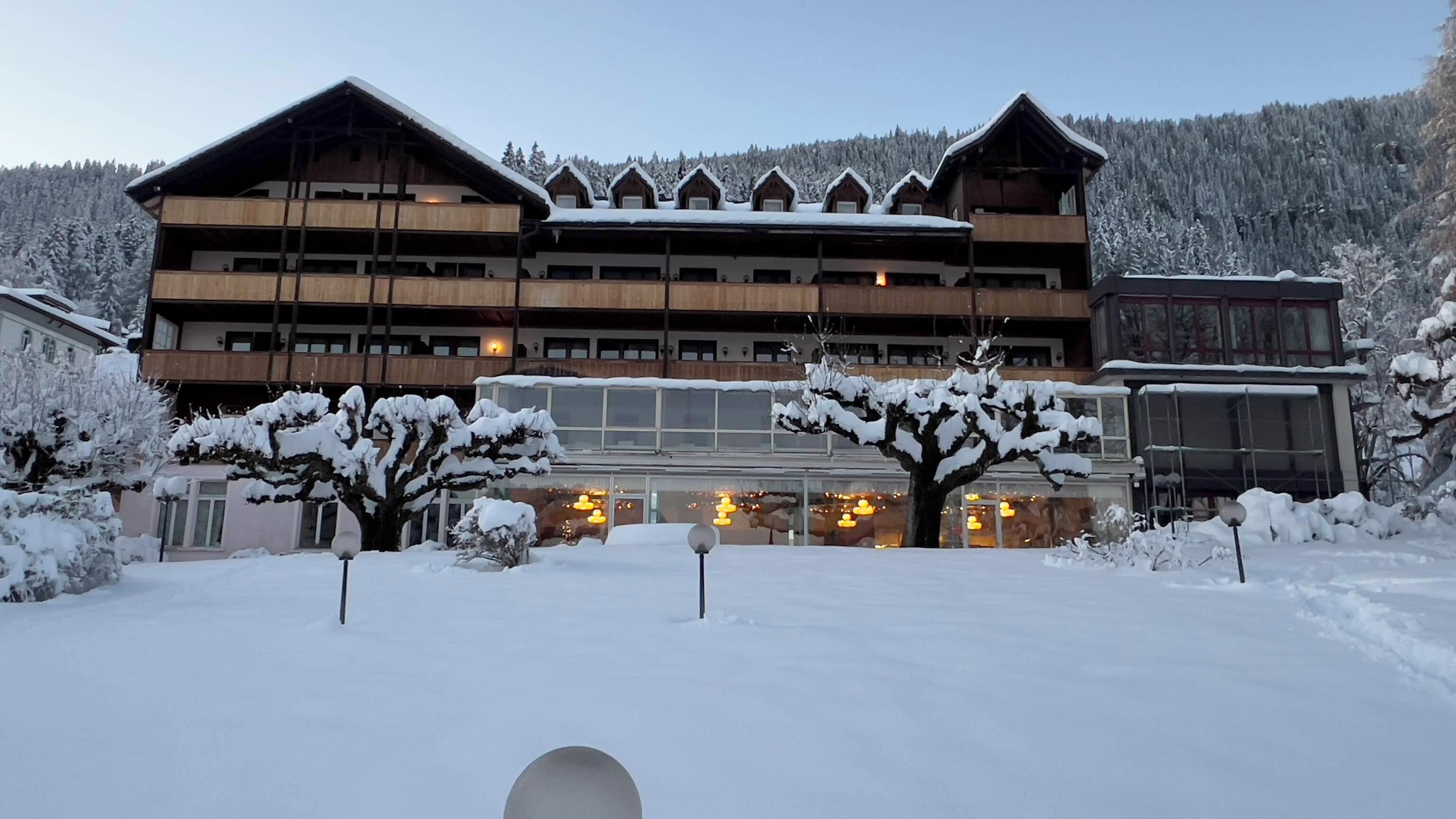 A multi-story wooden building with balconies, surrounded by snow-covered trees and a mountainous backdrop.